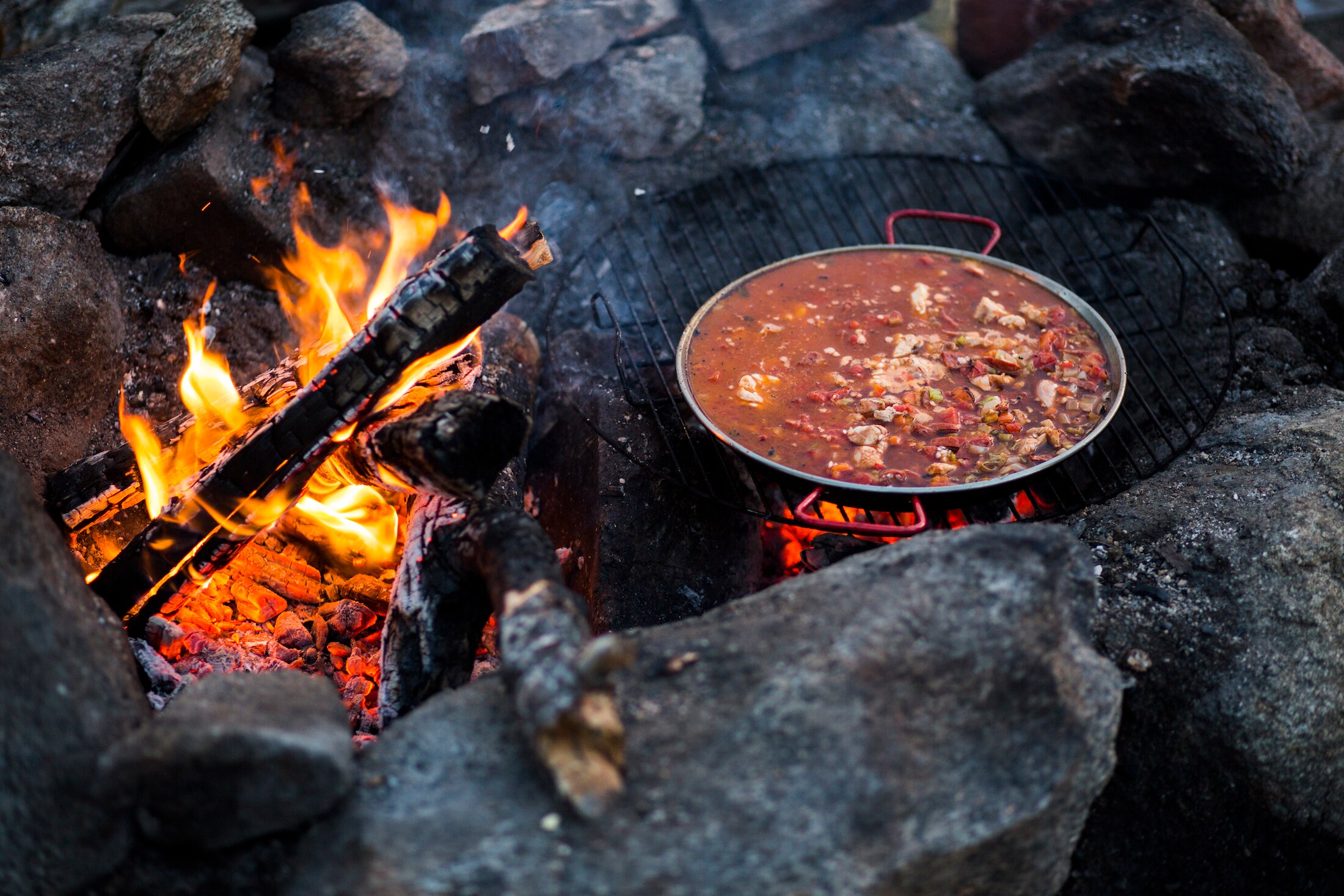 Pan of paella cooking over an open fire.