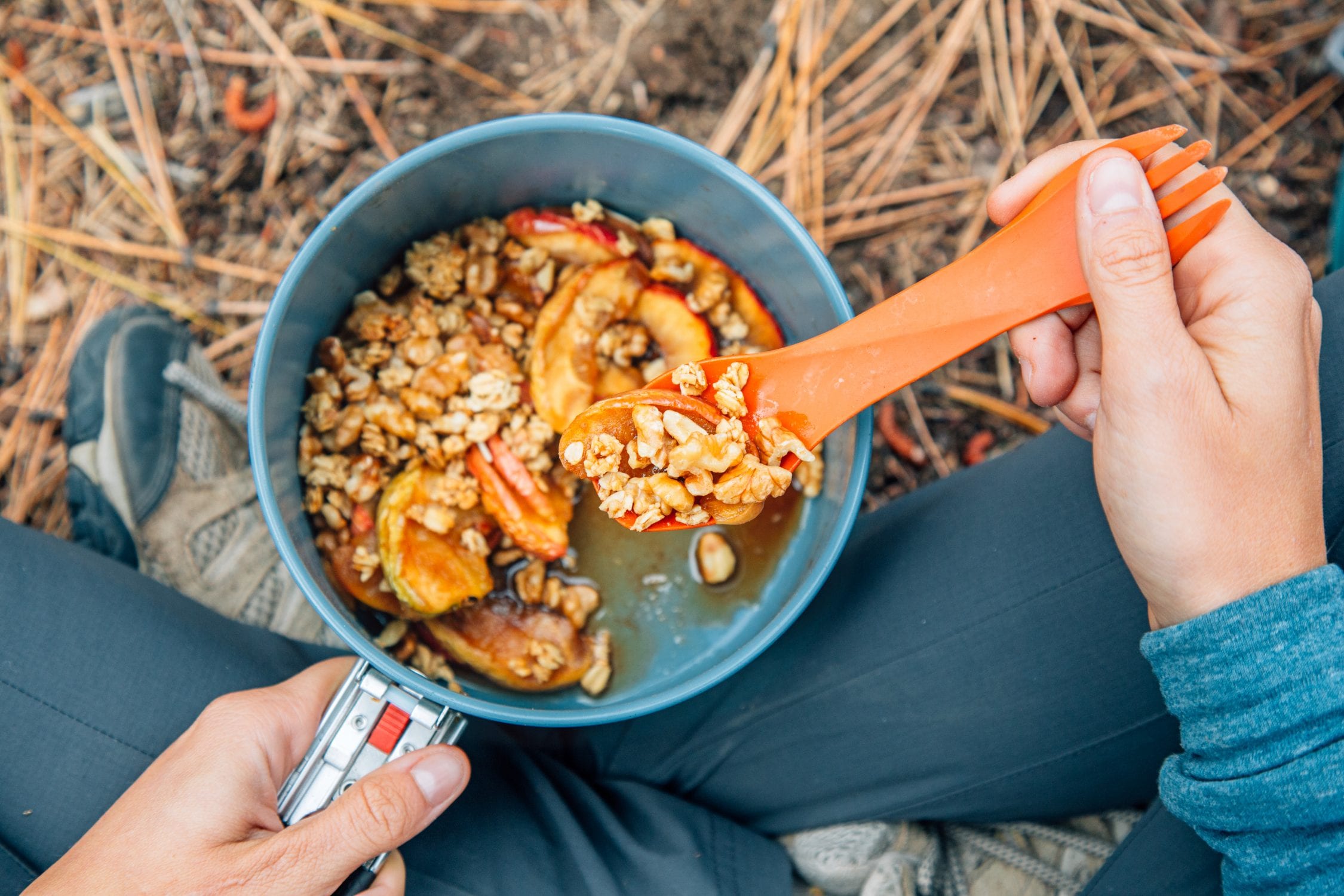 A person's hand scooping a spoonful of apple crisp out of a lightweight backpacking pot.