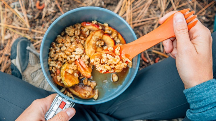 A person's hand scooping a spoonful of apple crisp out of a lightweight backpacking pot.