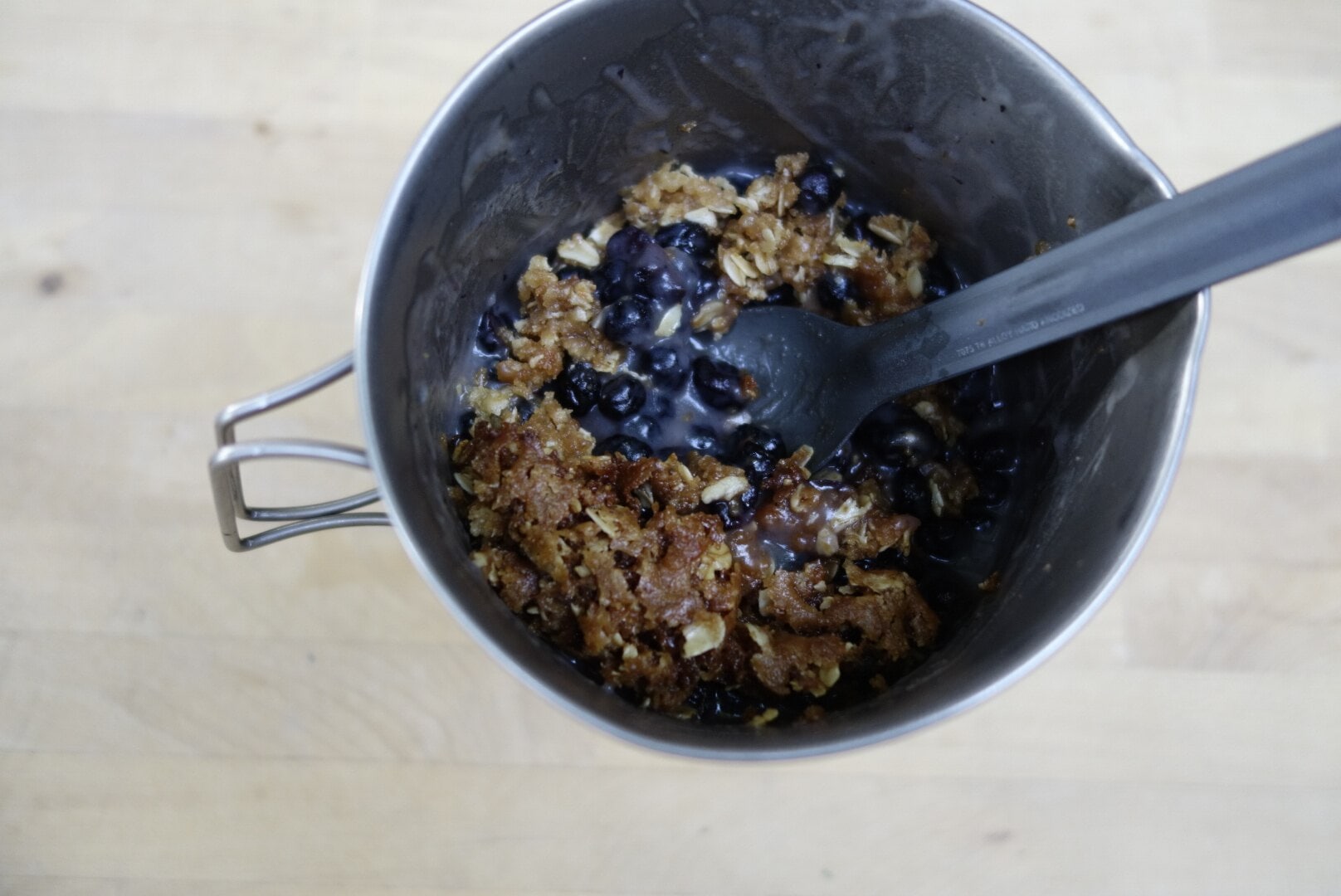 A cup with a spoon scooping out some blueberry crisp