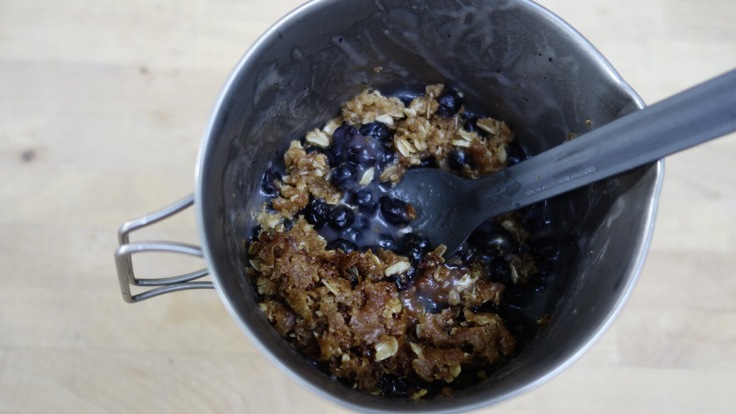 A cup with a spoon scooping out some blueberry crisp