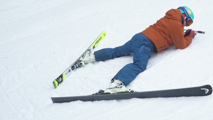 Photo of person lying in the snow with their skis on.