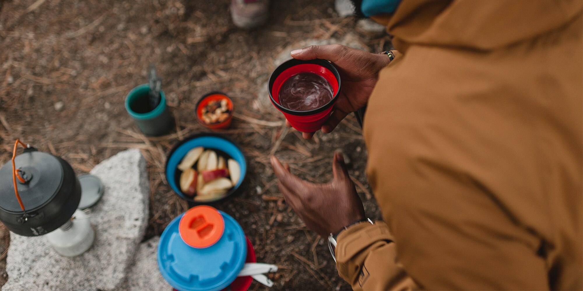 Person holds cup of coffee in the foreground. In the background there are snacks on the ground.