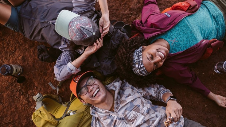 Three friends lay on the ground outside and laugh.