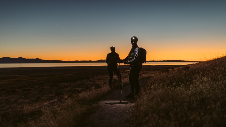 Two hikers on a trail at sunset.