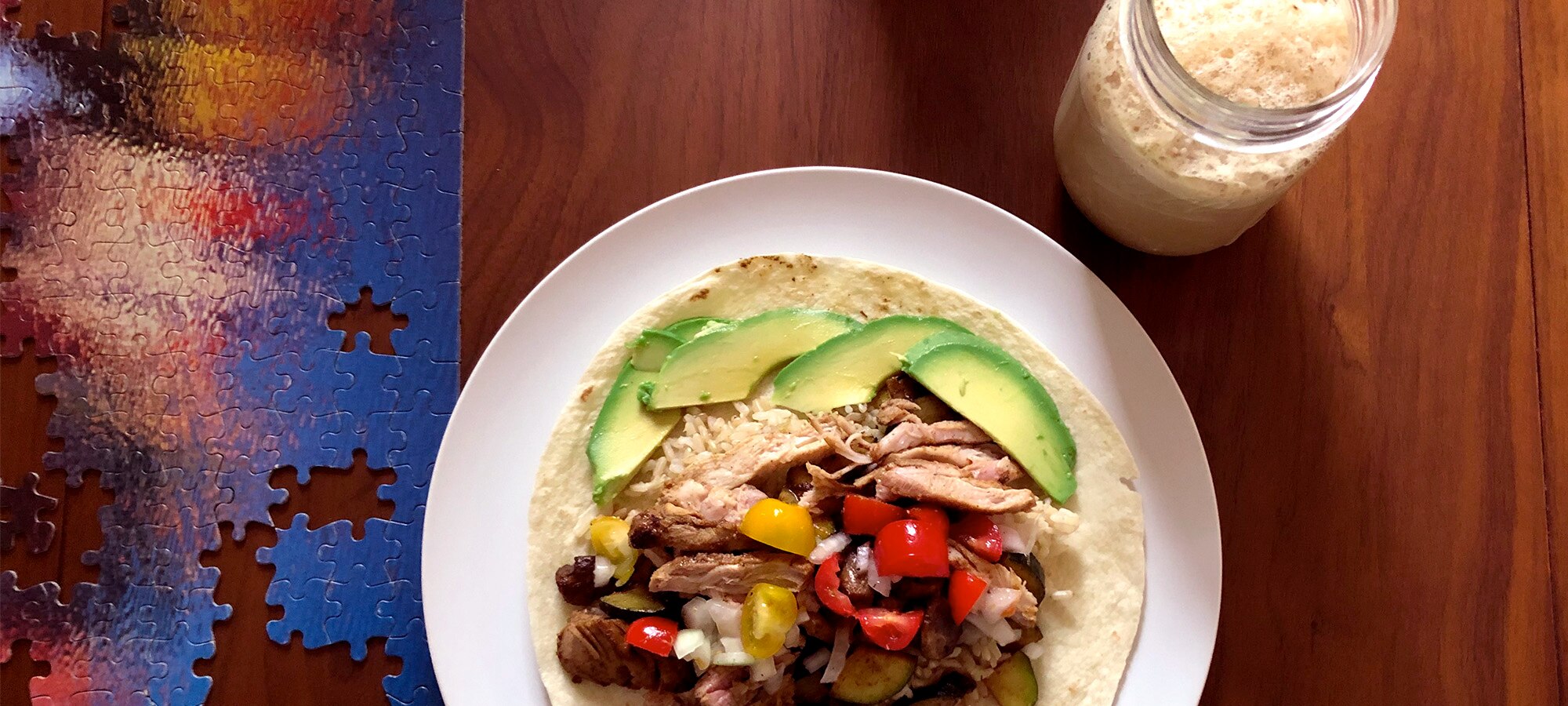 Chicken tacos on a white plate on a table with a puzzle and chai latte nearby