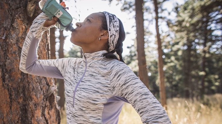 A trail runner pauses to take a drink from her water bottle.