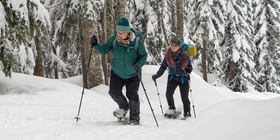 Two women snowshoeing on a path in the woods