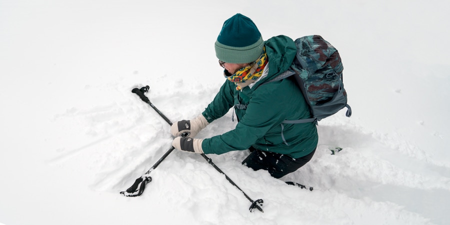 A snowshoer uses her poles to get back up after a fall