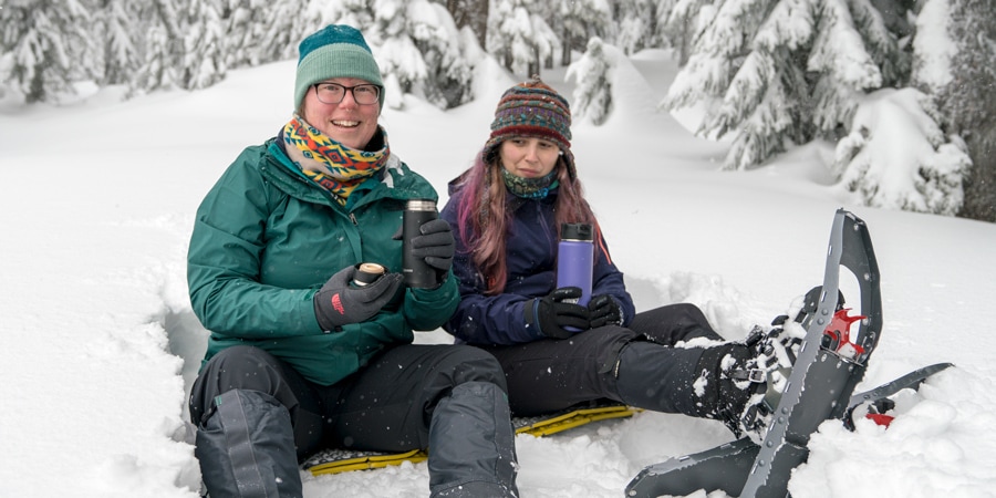 Two snowshoers take a break to drink hot beverages