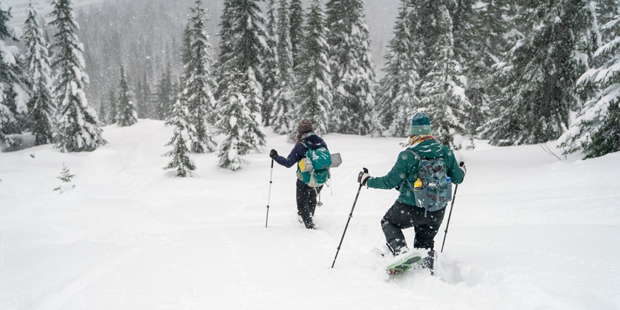 Two women snowshoeing down a steep hill