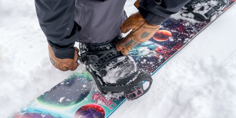 a snowboarder strapping into snowboard bindings