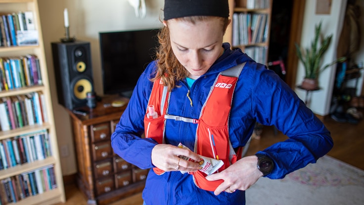 A trail runner puts an energy bar into the front pocket of her running vest before going for a run.
