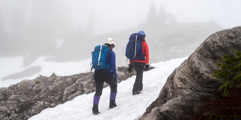 Two hikers walking up a snowy mountainside in the fog