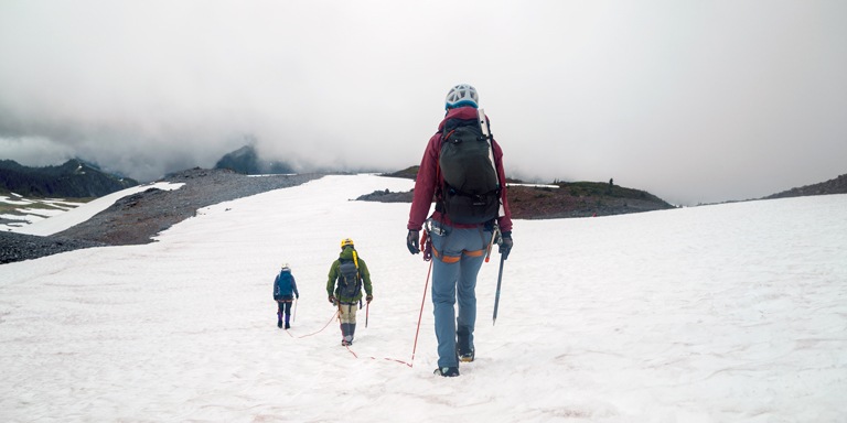 Three mountaineers on a roped team cross a snowy field