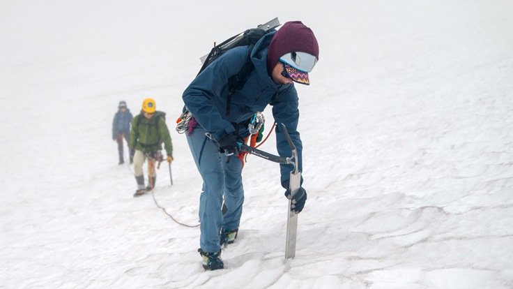 A mountaineer sets up a snow anchor using a vertical picket