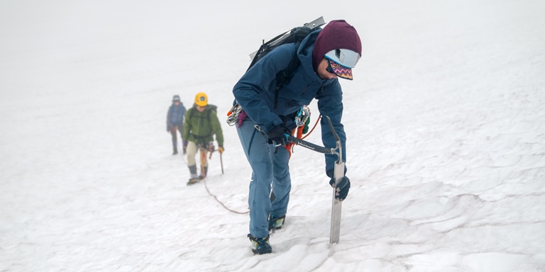 A mountaineer sets up a snow anchor using a vertical picket