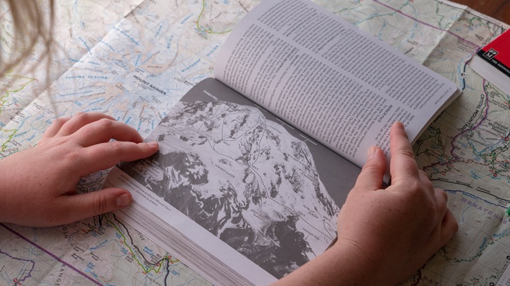 a climber planning their mountaineering route, with guidebook and map in hand