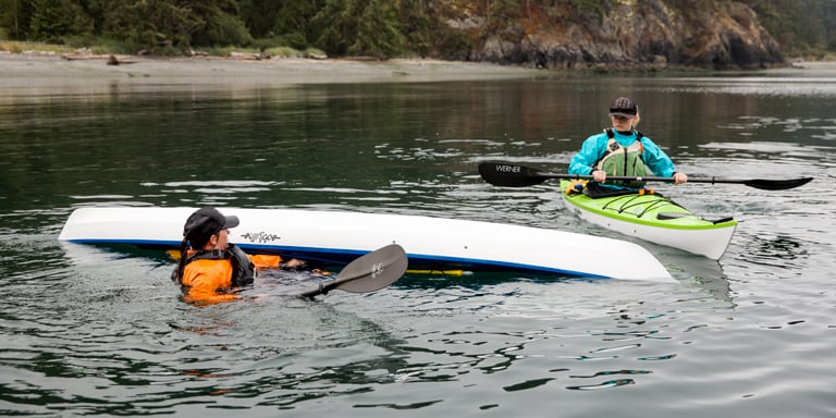 Instructor in the water with a flipped kayak as a student watches