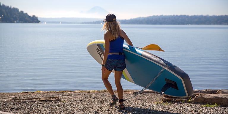 A woman carries her stand up paddle board towards water