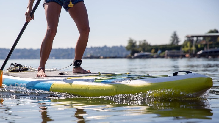 A paddle boarder uses their paddle to paddle through the water