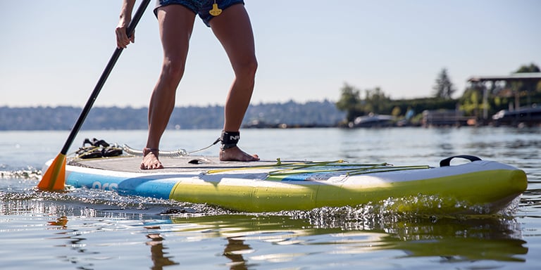 A paddle boarder uses their paddle to paddle through the water