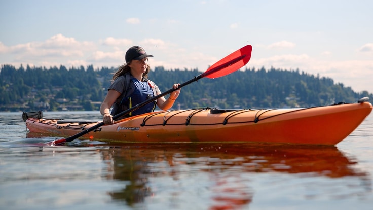 A woman paddles her kayak on a lake