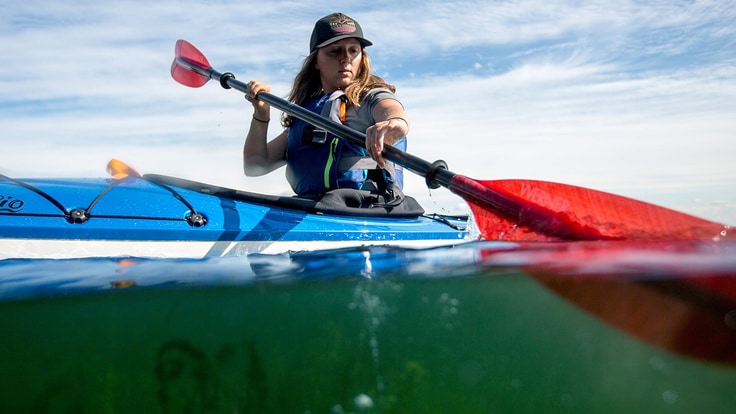 A woman paddles a kayak on a lake