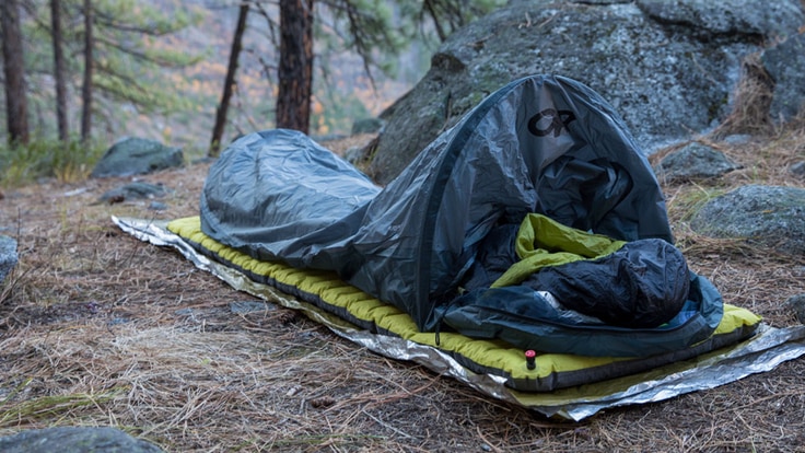 A bivy sack on top of a sleeping pad in a clearing in the woods