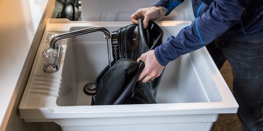 A man cleans a wetsuit in a large sink