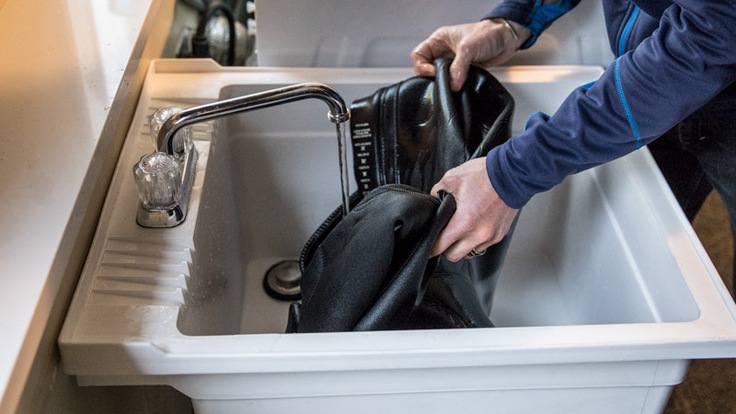 A man cleans a wetsuit in a large sink