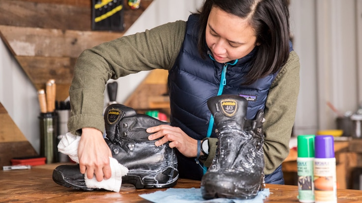 A woman cleaning and conditioning leather hiking boots