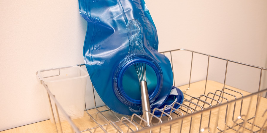 A hydration bladder drying on a rack while propped open with a kitchen whisk