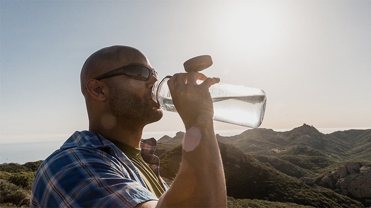 Person outside drinking from a plastic water bottle.