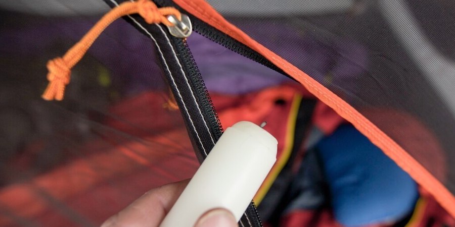 Detail photo of hands holding a candle against the teeth of a tent zipper