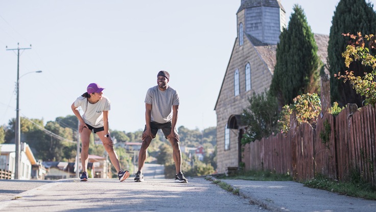 Two runners pause for a breath on a paved road where they've been running.