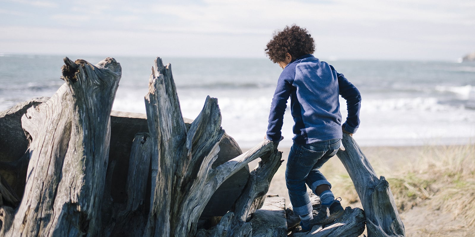 Child climbing on driftwood at the beach